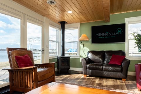 Cozy living room with leather furniture, a wood stove, and large windows overlooking a lake.