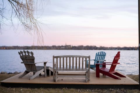 Wooden deck by the lake with colorful chairs and a serene sunset sky.