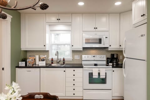 A modern kitchen with white cabinets, dark countertops, and a green accent wall, showcasing appliances and decorative items.