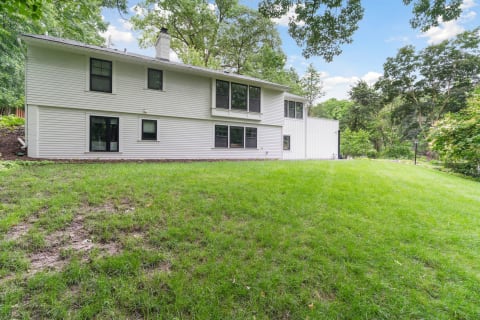 A two-story white house with large windows on a green lawn, set in a tranquil outdoor environment.