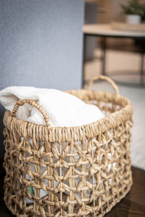 Wicker basket with a white blanket inside on a wooden surface in a softly blurred room.