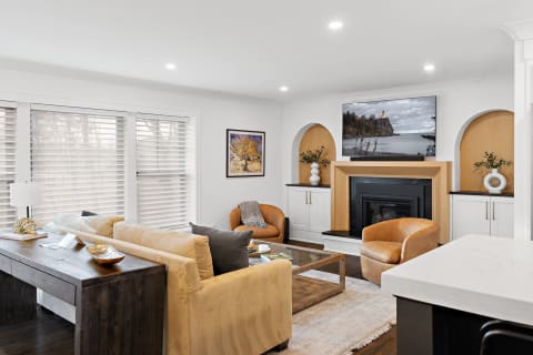 Contemporary living room with beige sofa, leather chairs, and a mounted TV over a fireplace.