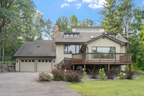 A lovely house with a wooden deck and garage, set against a backdrop of trees.