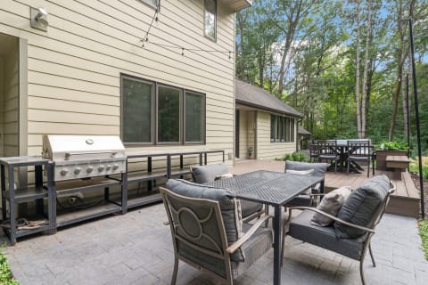 Outdoor patio area with a grill and seating, surrounded by trees and greenery.