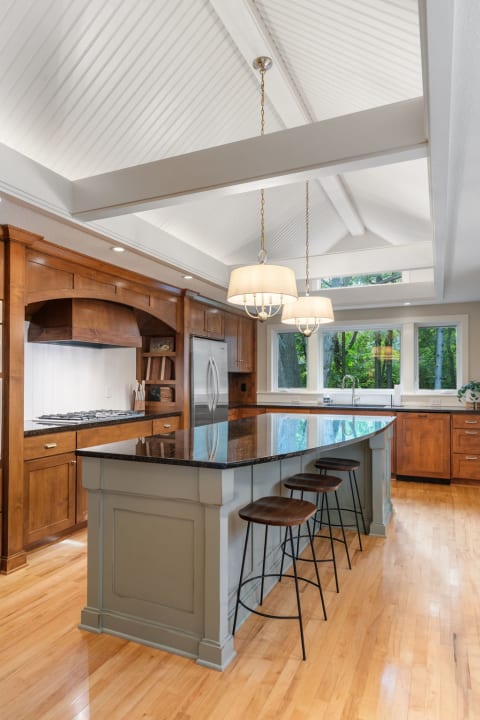 A modern kitchen featuring a high vaulted ceiling, an island with a dark granite countertop, and warm wooden cabinetry.