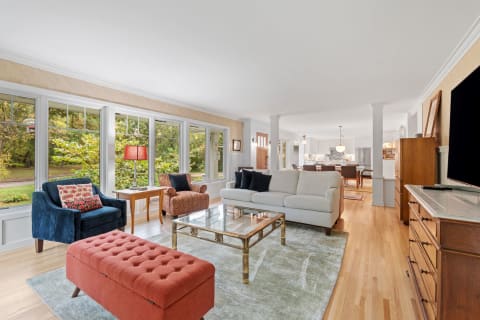 Spacious living room with large windows, colorful furniture, and an open layout to the dining area.
