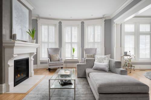 Unwind in your elegant living room with soft gray tones, cozy fireplace, and abundant natural light from floor-to-ceiling windows.