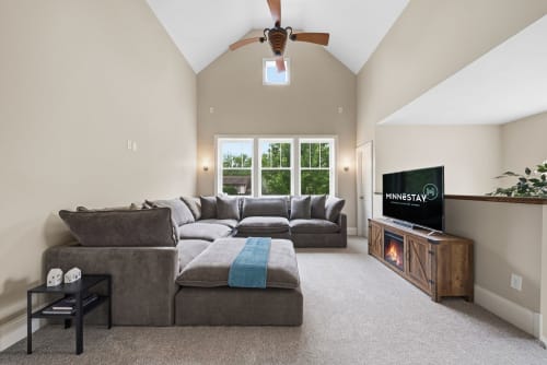 Sink into plush seating beneath soaring vaulted ceilings. Natural light floods through tall windows as you unwind with entertainment or the gentle warmth of the fireplace.