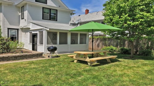 Spacious backyard with picnic table, BBQ grill, and umbrella shade for perfect outdoor dining and relaxation during your stay.