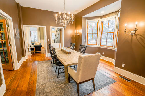 Your elegant dining room glows with warm chandelier light, where rich hardwood floors and sophisticated furnishings create the perfect space for memorable meals.