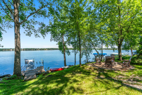 Peaceful lakefront setting with mature trees creating natural shade over the waterfront seating and dock area.