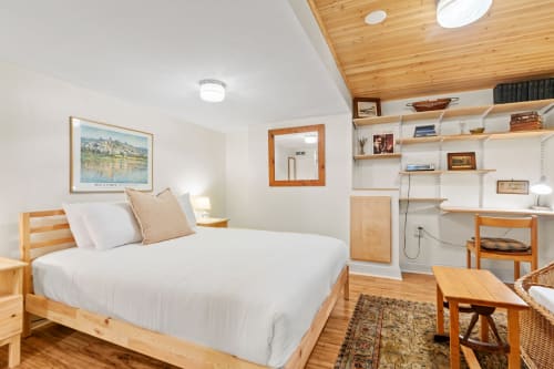 A cozy, minimalist bedroom featuring a wooden bed, warm lighting, and a touch of art.