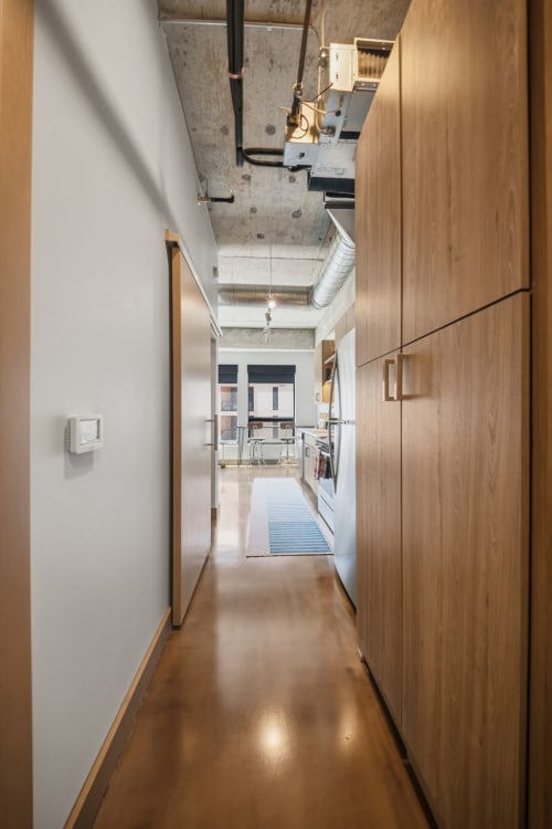 Industrial-chic hallway with exposed concrete ceilings and sleek wood cabinetry leads to your bright, modern kitchen beyond.