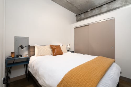 Unwind in your industrial-chic bedroom with exposed concrete ceilings and crisp white linens accented by warm terracotta touches.