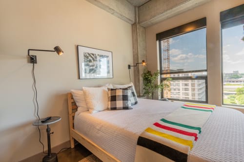 Sink into your comfortable bed with city views stretching beyond the window, where modern lighting and thoughtful touches create your perfect urban retreat.