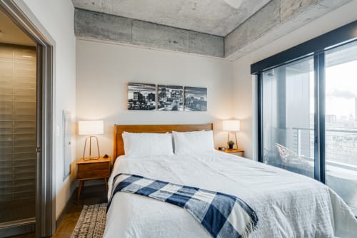 Sink into crisp linens and wake to stunning city views in your modern bedroom with industrial charm and warm wood accents.