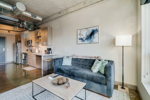 Relax in your modern loft featuring a plush blue sofa, sleek coffee table, and open kitchen with premium appliances.