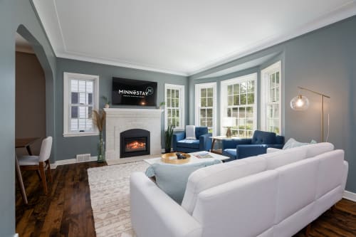 Unwind in this elegant living room where soft blues meet crisp whites, warmed by a cozy fireplace and filled with natural light.