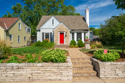 Charming cottage with stone accents and bright red door creates a welcoming entrance in this peaceful neighborhood setting.