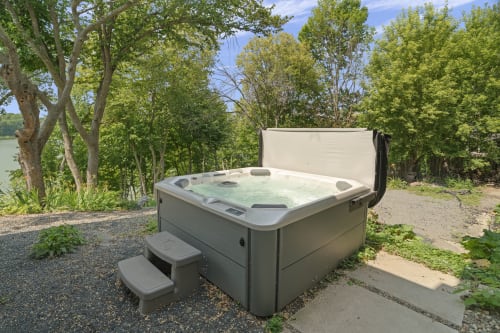 Soak in your private hot tub surrounded by lush trees, with peaceful water views stretching beyond the leafy canopy—a perfect spot to unwind.