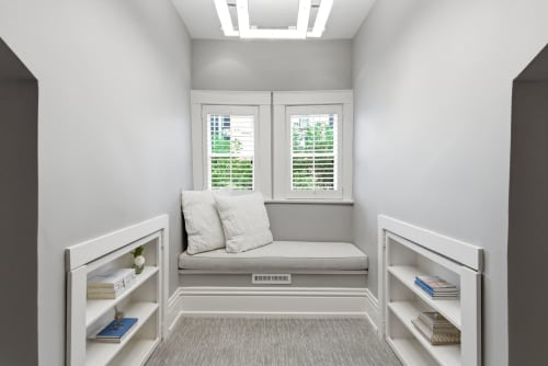 Your perfect reading spot awaits: a cozy window bench with soft cushions and natural light streaming through plantation shutters, framed by built-in shelves for your favorite books.