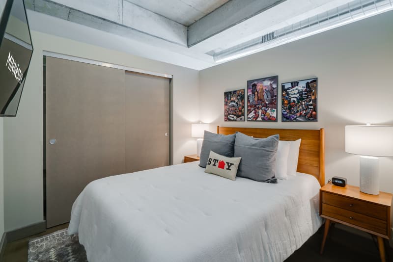 Sink into crisp white linens and plush pillows in your modern bedroom, where exposed concrete meets warm wood and colorful artwork creates your urban retreat.