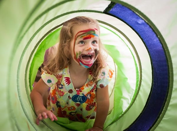 Young girl with facepaint crawling through a tube.